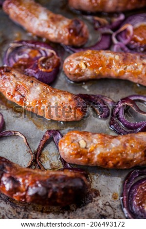 Baking tray with six baked pork and apple sausages covered with red onions and mango chutney. Shallow depth of field