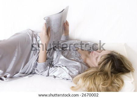 A women in a silver silk robe holding a magazine and reading