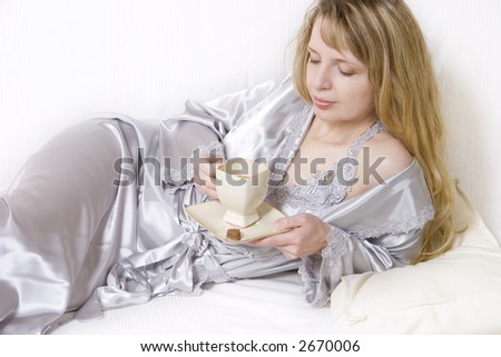 A women in a silver silk robe, lying on the sofa enjoying a coffee