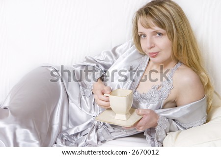 A women in a silver silk robe holding a cup of coffee on the sofa