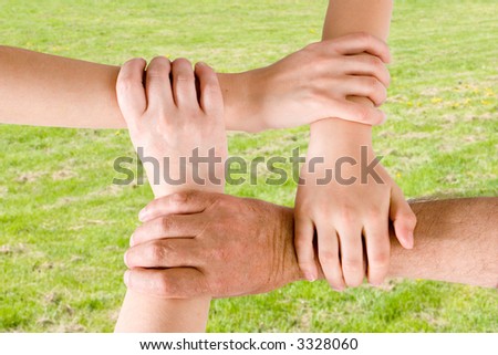 Four hands joined together with a grass background