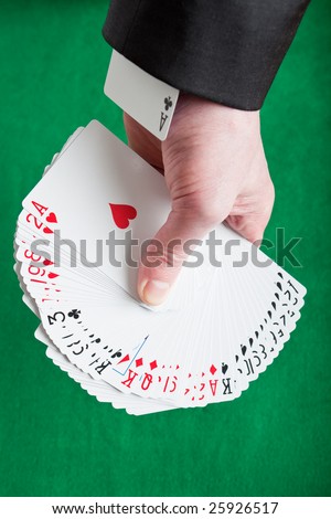A fan of mixed playing cards on a green felt background with an ace up the sleeve