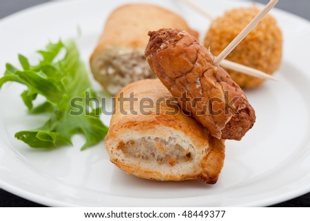 Small party snacks containing sausage rolls, a scotch egg and a cocktail sausage on a white plate