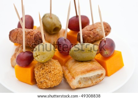 Party snacks. Mini sausage rolls, olives, scotch eggs, cheese and red grapes on white plates