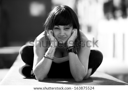 Portrait of beautiful young girl in urban background. Sitting in the floor. Black and white image.