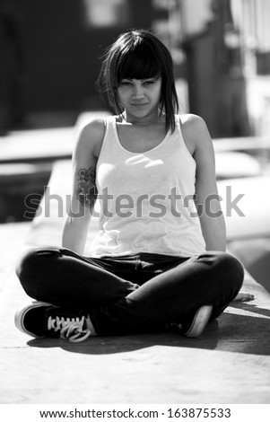 Portrait of beautiful young girl in urban background. Sitting in the floor. Black and white image.