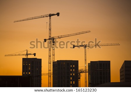 Cranes at sunset. Industrial construction cranes and building silhouettes over sun at sunrise.