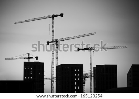 Cranes at sunset. Industrial construction cranes and building silhouettes over sun at sunrise. Black and white image.