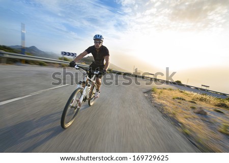 Cyclist man riding mountain bike in sunny day on a mountain road. Image with flare.