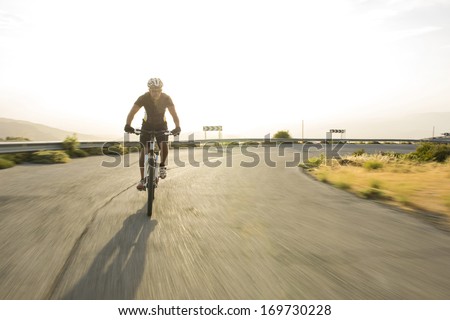 Cyclist man riding mountain bike in sunny day on a mountain road. Image with flare.