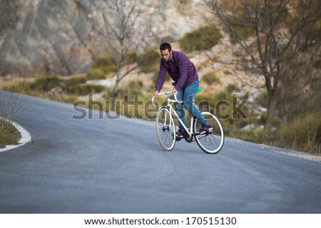 Cyclist man riding fixed gear sport bike in sunny day on a mountain road