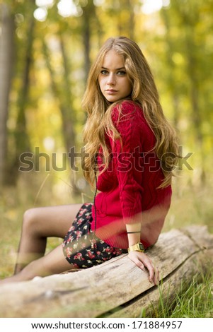 Portrait of a young blonde female on field  sitting on a tree trunk.