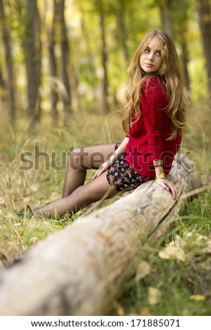 Portrait of a young blonde female on field  sitting on a tree trunk.