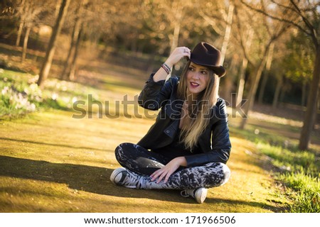 Portrait of a beautiful woman in hat on the park sitting on the floor.