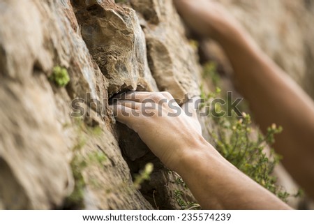 Rock climber's hand grasping handhold on natural cliff. His hand is covered in chalk. Shallow depth of field.