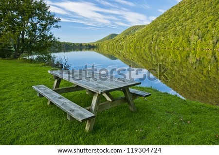 Picnic table beside river with green grass and forest reflection in Cape breton highlands