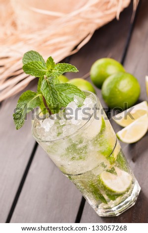 Lime Mojito cocktail with a straw hat on a wooden table, a Cuban cocktail made with cuban rum, lime, sugar and a splash of soda