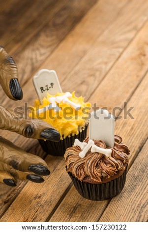 Werewolf hand reaching for a Halloween cupcake on a rustic wooden table close up