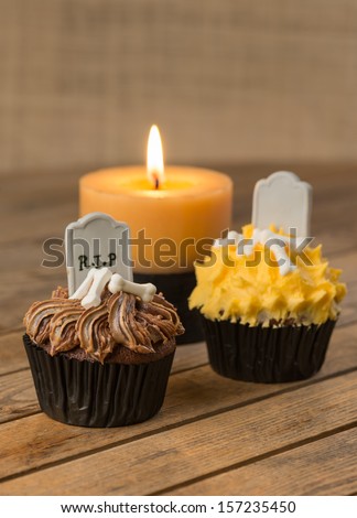 Halloween cupcakes with tombstone cake topper and a burning candle on a rustic wooden table close up