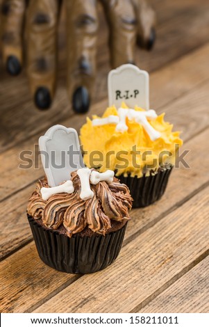 Werewolf hand slowly reaching for the Halloween cupcakes with tombstone cake topper close up