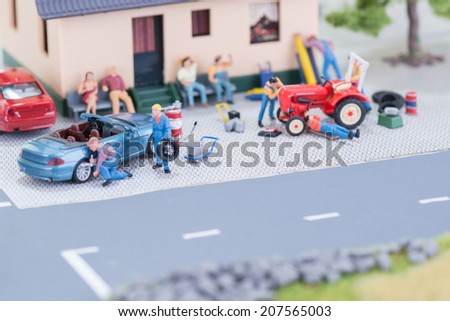 Miniature mechanics repairing a convertible car and a farm tractor close up