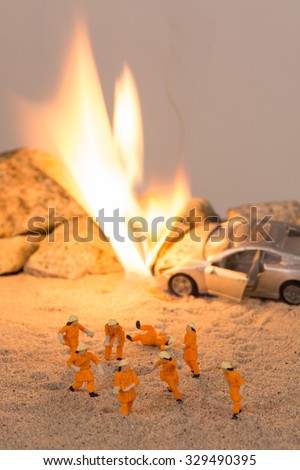 Miniature firemen at a car accident scene in flames