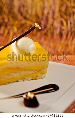 French custard cake with chocolate stick and edible gold leaf on a white plate