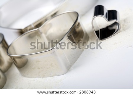 Some metal heart-cookie-cutters with some flour on white background. Tilt view. 2