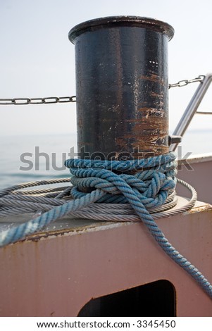 Detailshoot of a ship: Worn Naval rope tied up. Sea in the background.