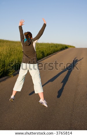 Woman from behind in sporty clothes. Cuts a caper - jumps into the air. Picture from behind with long shadow on the street.