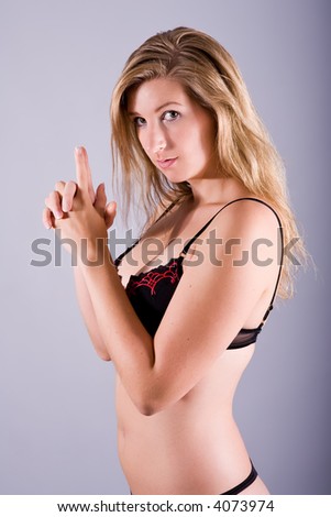 Young woman in underwear with both hands formed to a gun and seems to be ready to shoot. View from side.