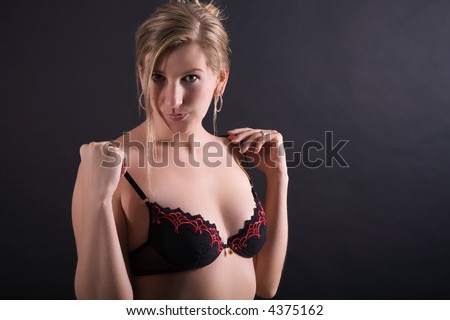 Young woman holds her Bra and takes it off soon. Maybe. Dark background. Strand of hair in face.