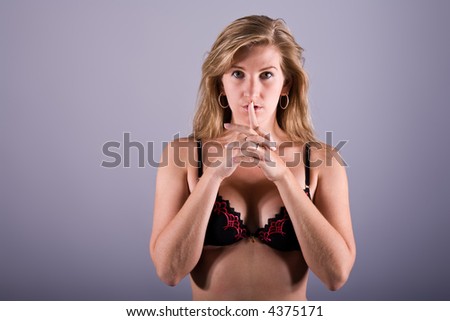 Young sexy woman in underwear with both hands formed to a gun on grey background.