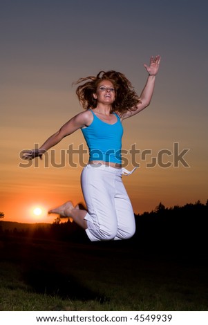 Nice redhaired woman with freckles jumps up while being barefoot. Sun goes down in the background.