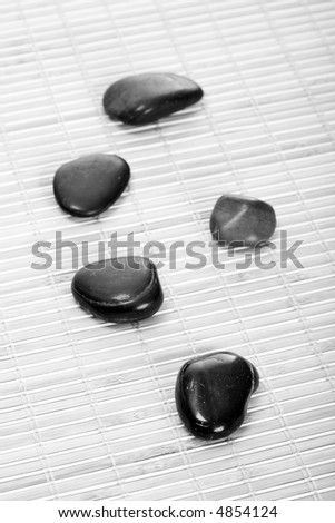 Five smooth, black Zen-Stones (Pebbles) in a row on a bamboomat. Focus on front stone. Black-white.