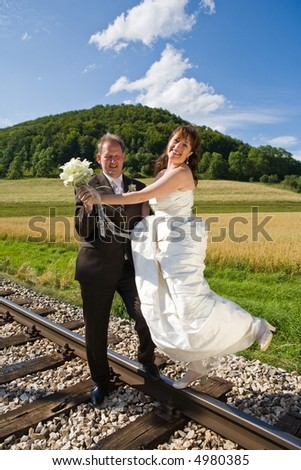 Bridal couple on rails, being in the nature. Great azure sky. Great summer! She balances on one foot on the rail.