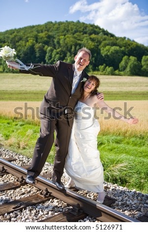 Bridal couple on rails, being in the nature. Great azure sky. Great summer! He balances on one foot on the rail.. They have fun.