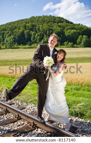 Bridal couple on rails, being in the nature. Great azure sky. Great summer! He balances on one foot on the rail.