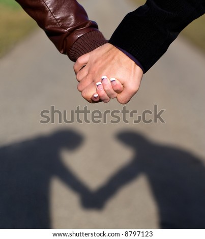 Shadow of couple heartshaped. Two hands holding each other outdoor. Focus on hands, blurred way.