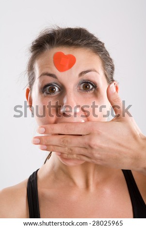 Woman with surprised look holding hand over her mouth and wearing a heart on her forehead.