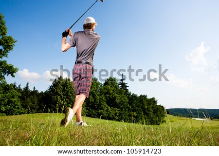 Male golf player teeing off golf ball from tee box with clean blue sky background
