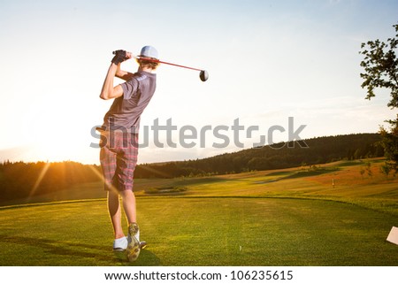 Male golf player teeing off golf ball from tee box to beautiful sunset