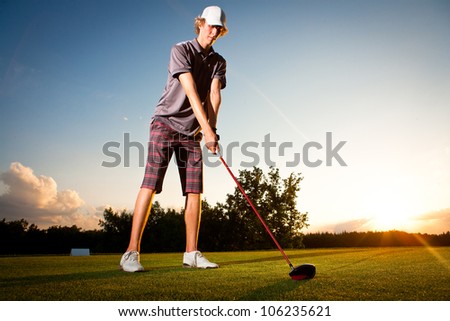 Male golf player teeing off golf ball from tee box to beautiful sunset