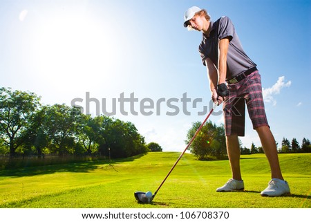 Male golf player teeing off golf ball from tee box with clean blue sky background