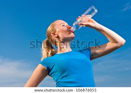 young female athlete drinking water to refresh during a hot weather running/training, blue sky background