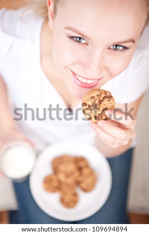 Cute young woman eating cookies and drinking milk, vertical picture from above, model is smiling into the camera