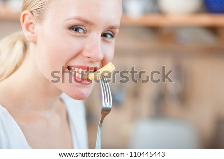 Woman tasting cooked macaroni in the kitchen, preparing mac and cheese