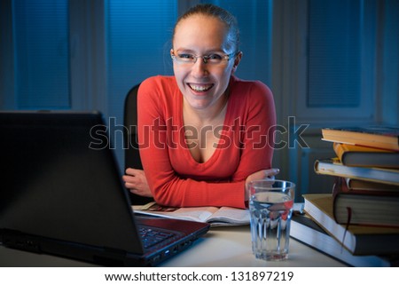young  happy female college student smiling behind her table on a late evening,  funny night procrastination concept