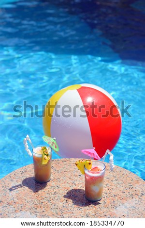 Two cocktail glasses and a water ball by a blue water of swimming pool (you text on top of the image)