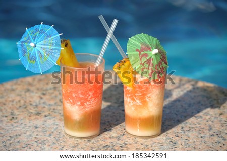 Two cocktail glasses on a marble table by a blue water of swimming pool